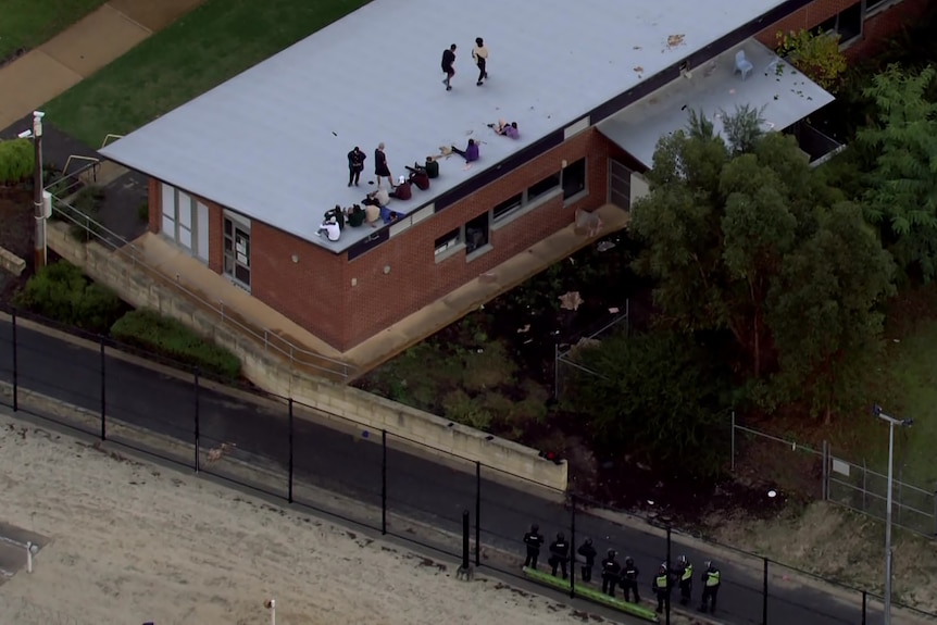 An aerial shot showing detainees on the roof of a building at Banksia Hill Detention Centre, with armed officers on the ground.