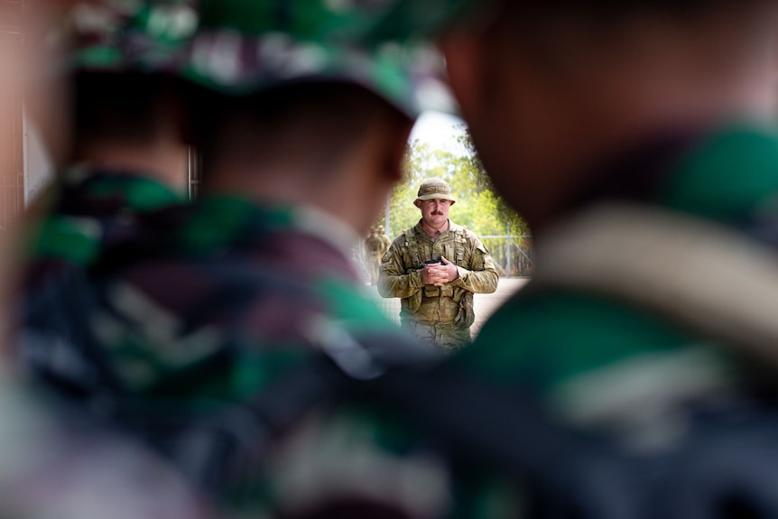 An Australian soldier in camouflage, seen from behind a row of Indonesian soldiers