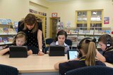 Primary school students use laptops in the library.