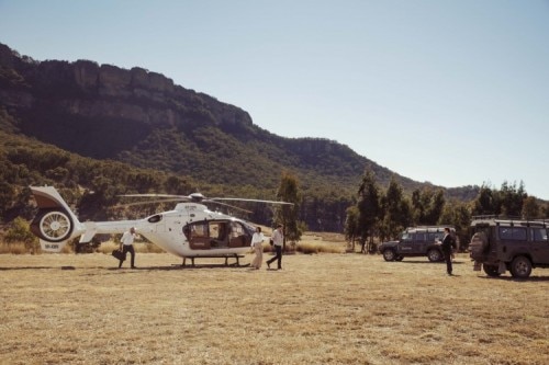 People step off a helicopter into 4wd vehicles