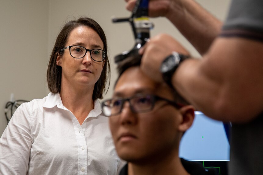 Woman with dark hair and glasses watching medical scan conducted on young man in lab