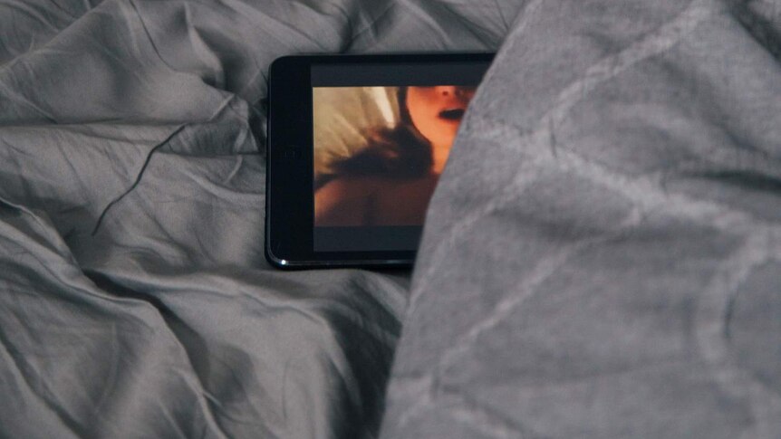 An image of a porn video displayed on a phone, obscured by bed sheets