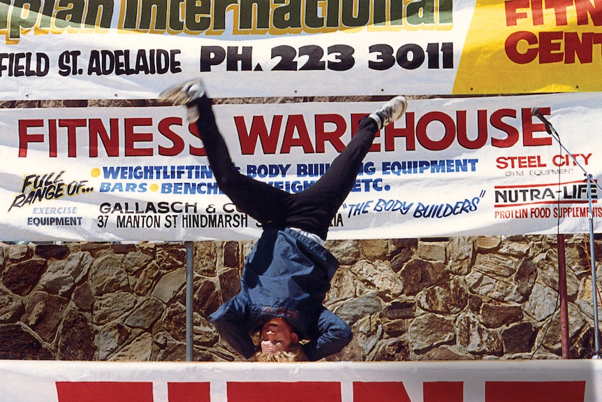 A young boy spins on his head in front of advertising banners