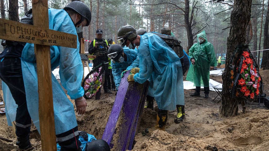 Emergency workers move a box containing a body of a civilian during the exhumation.