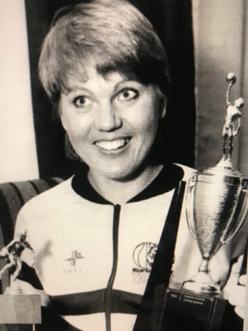 A black and white image of a woman holding several trophies and smiling.