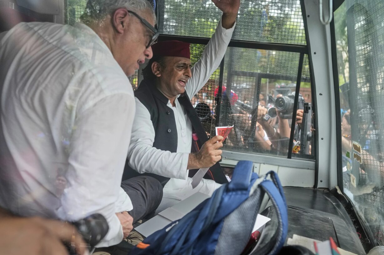 An Indian lawmaker sitting at the back of a police van, waving to a crowd