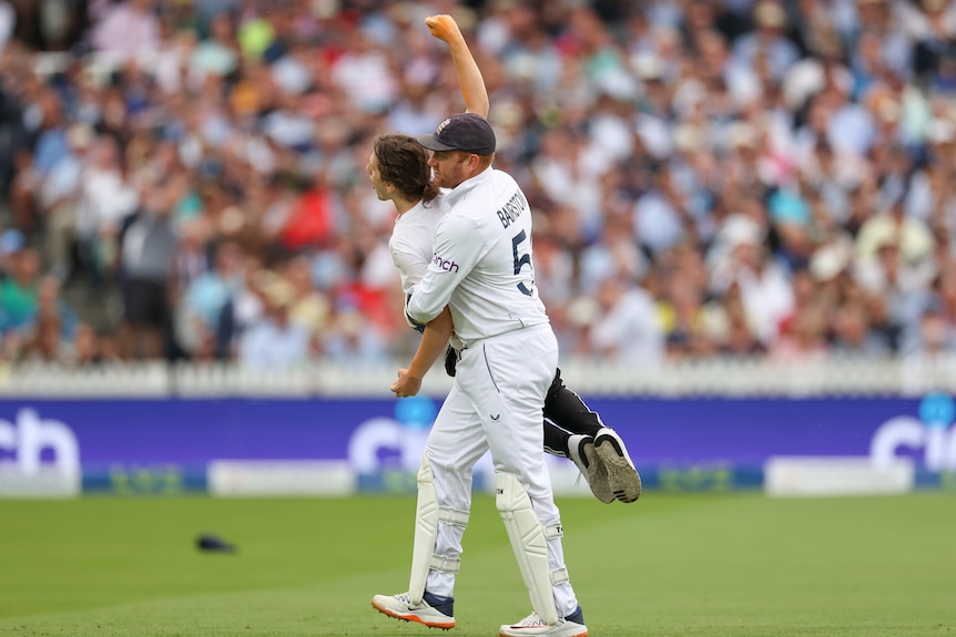 A cricket player in whites carries a protester off the ground.
