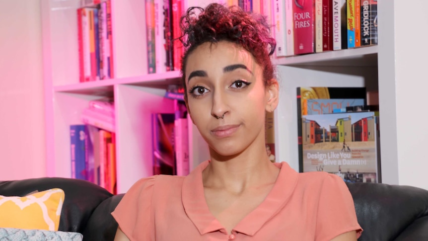 Young woman sits in front of a bookshelf which is lit with a purple light.