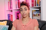 Young woman sits in front of a bookshelf which is lit with a purple light.