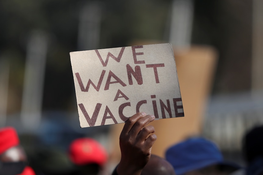 A person holds up a placard reading 'We Want a Vaccine' 