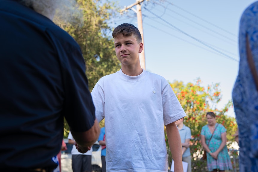 A teenage boy wearing a white T-shirt shakes hands 