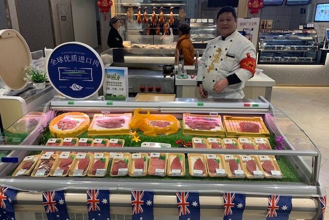 A butcher stands behind a cabinet of Australian beef, adorned with Australian flags.