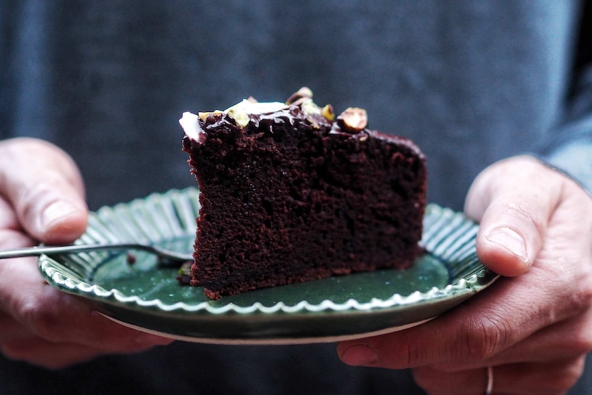Close up of a slice of chocolate olive oil cake on a plate being held by hands.