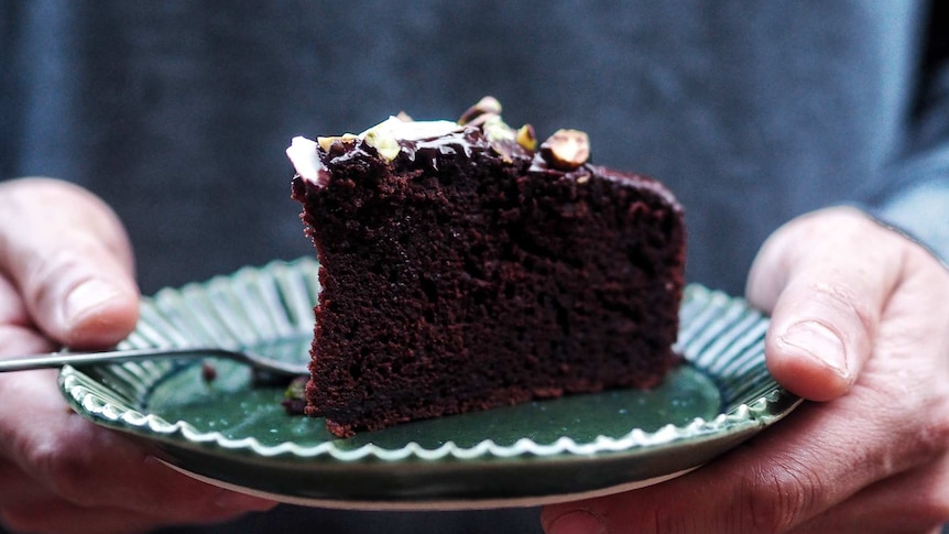 Close up of a slice of chocolate olive oil cake on a plate being held by hands, a delicious dessert recipe.