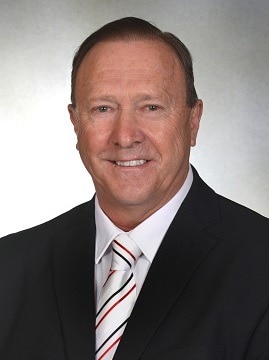 Wearing a suit and tie, Geoff Ablett smiles as he poses for a portrait