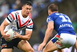 A Sydney Roosters NRL player holds the ball in two hands as he approaches a Warriors opponent.