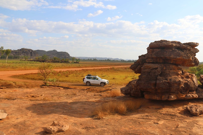 A white four wheel drive parked in the wide open red dirt landscape