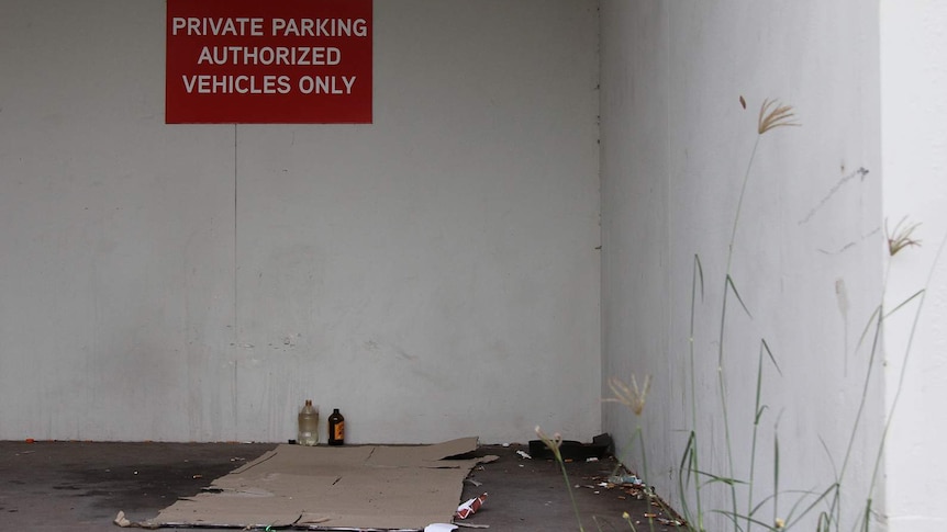 A rough sleeping hot-spot with a flattened cardboard box, some abandoned clothes and glass bottles.