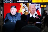 Commuters watch a TV showing a file image of North Korean leader Kim Jong-un and US President Joe Biden.