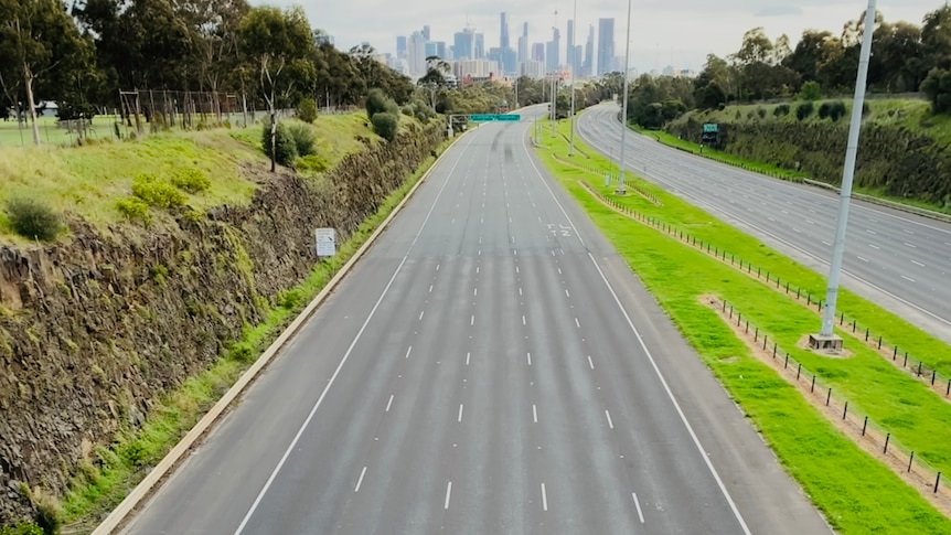 Empty city-bound lanes from the East Highway, viewed from an overpass, with the CBD skyline visible ahead.