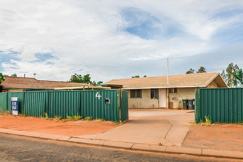 A wide shot of a house in a country town behind a green fence.