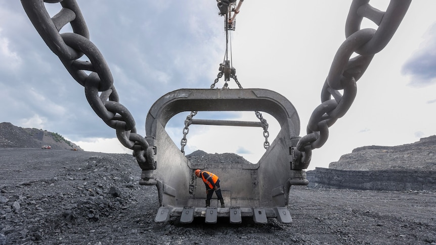 A man in an orange high-vis vest inspecting a giant bucket at a coal mine