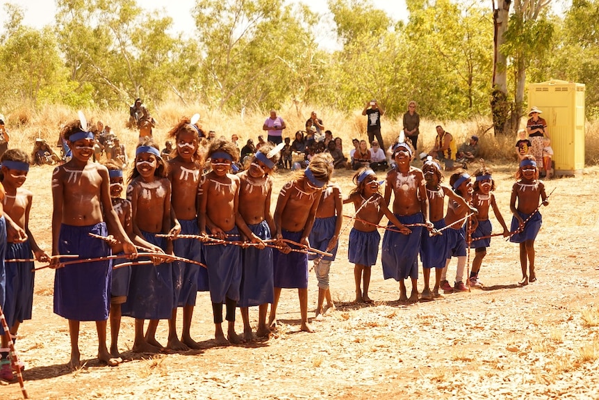 Aboriginal children wear blue skirts and feathers in their hair