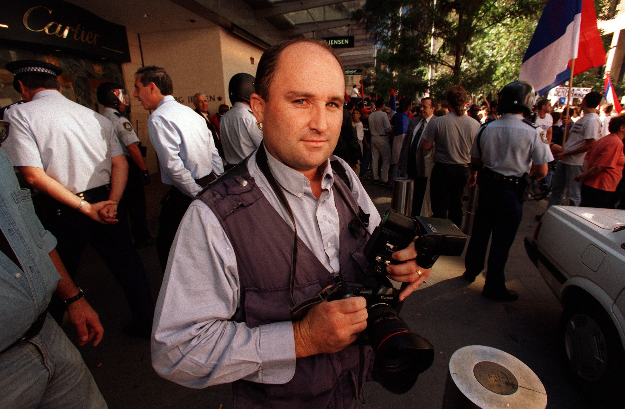Man holding a camera with a crowd in the background.