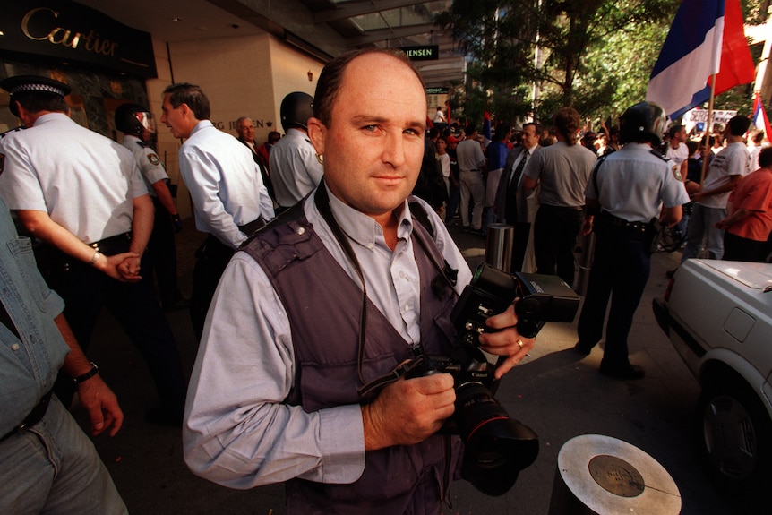 Man holding a camera with a crowd in the background.