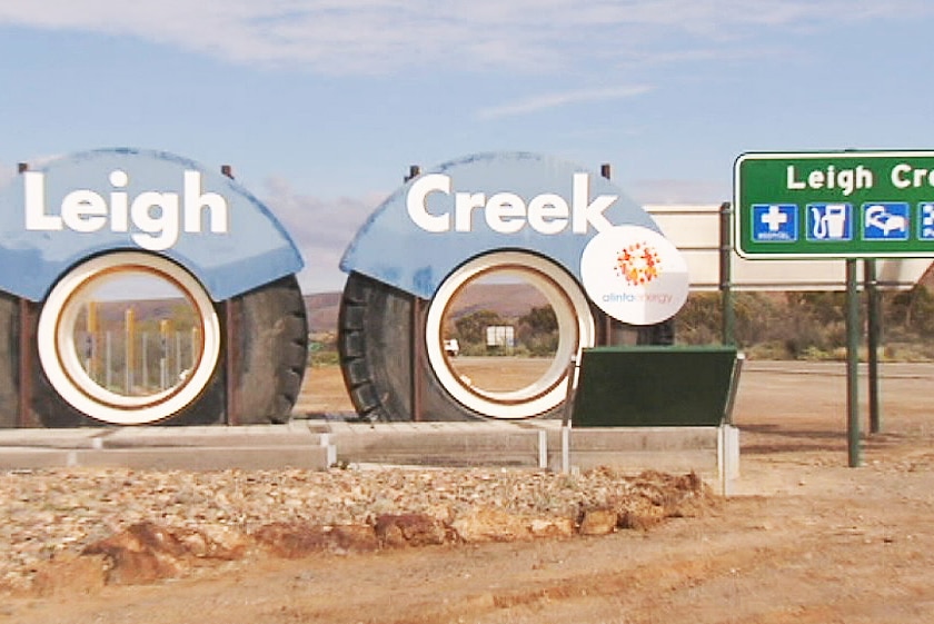 Two big tyres with the words Leigh and Creek next to a road sign.