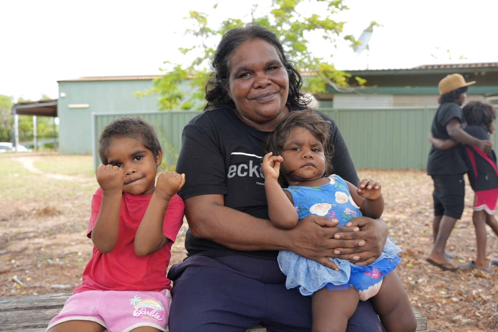 Mulher sentada e sorrindo com duas crianças pequenas, uma no colo e outra ao lado