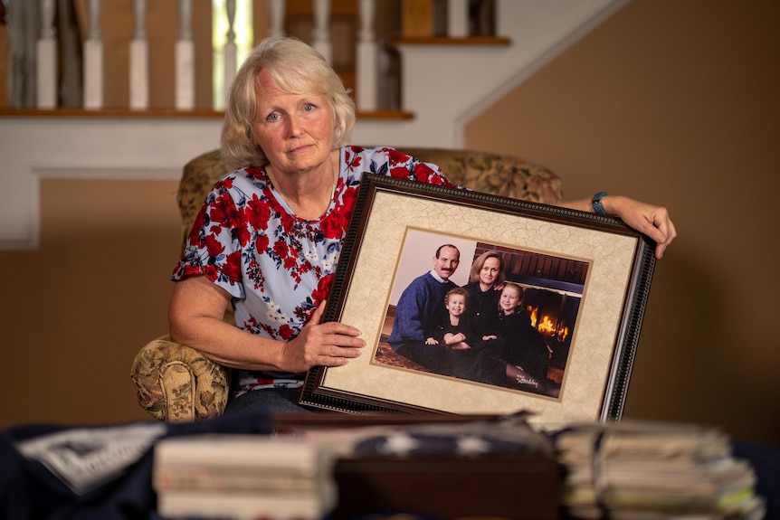 A woman holds a framed photograph of a family 