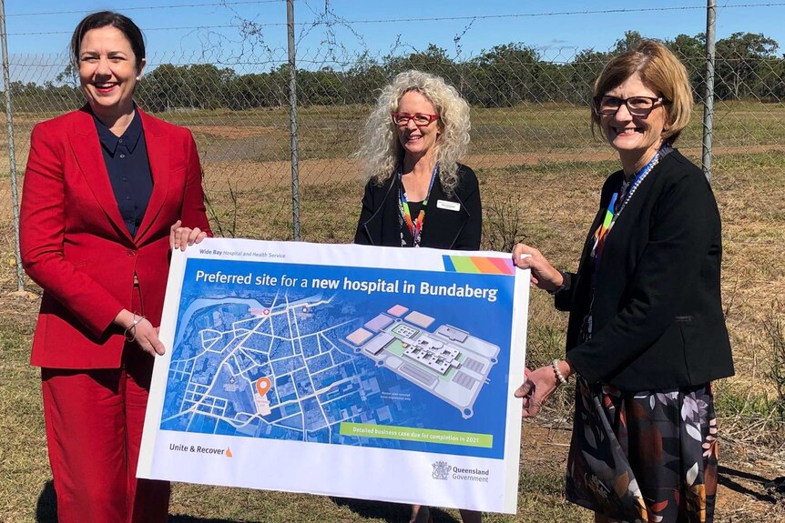 Three women in business attire hold a large cardboard map that reads "Preferred site for a new hospital in Bundaberg"