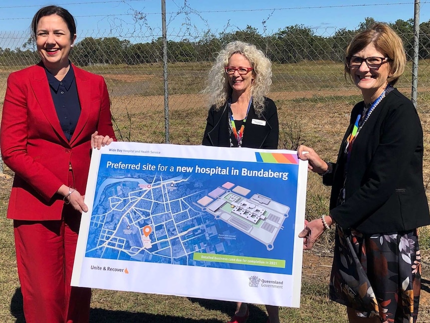 Three women in business attire hold a large cardboard map that reads "Preferred site for a new hospital in Bundaberg"