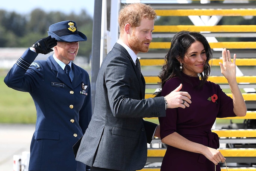 A woman waves and a man holds her shoulder