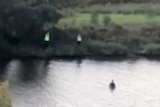 A screenshot of two police officers on a riverbank and a boy in the water.