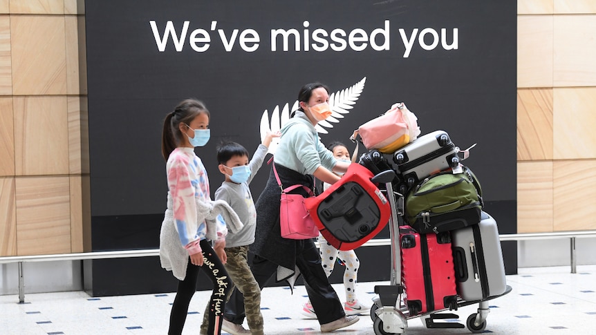 Four travellers wearing face marks, walking through Sydney International Airport with their luggage.