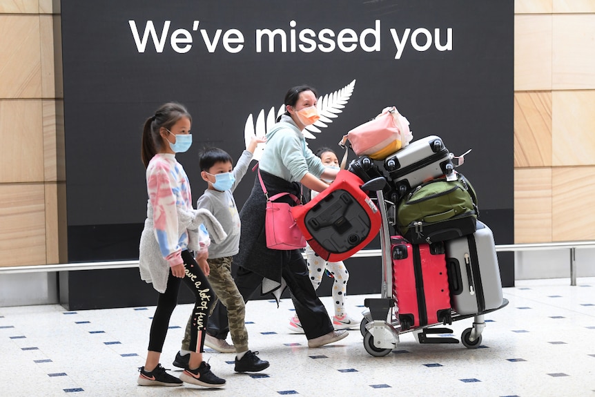Four travellers wearing face marks, walking through Sydney International Airport with their luggage.