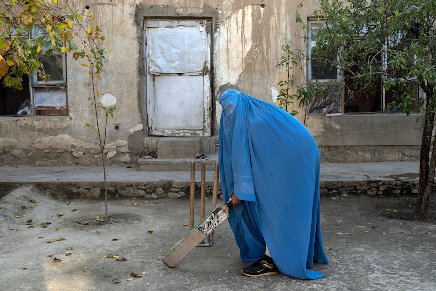一名身穿罩袍的阿富汗妇女拿着板球拍摆姿势拍照。
