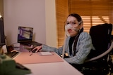 A lady with a ventilator sits at a computer while looking at the camera