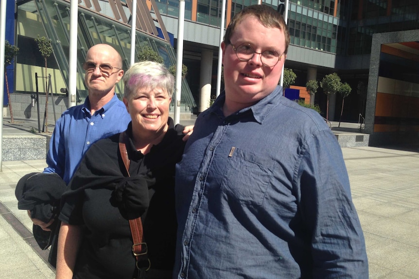 Liam McGarrigle smiles and hugs his mum, as his father stands behind him, outside court.