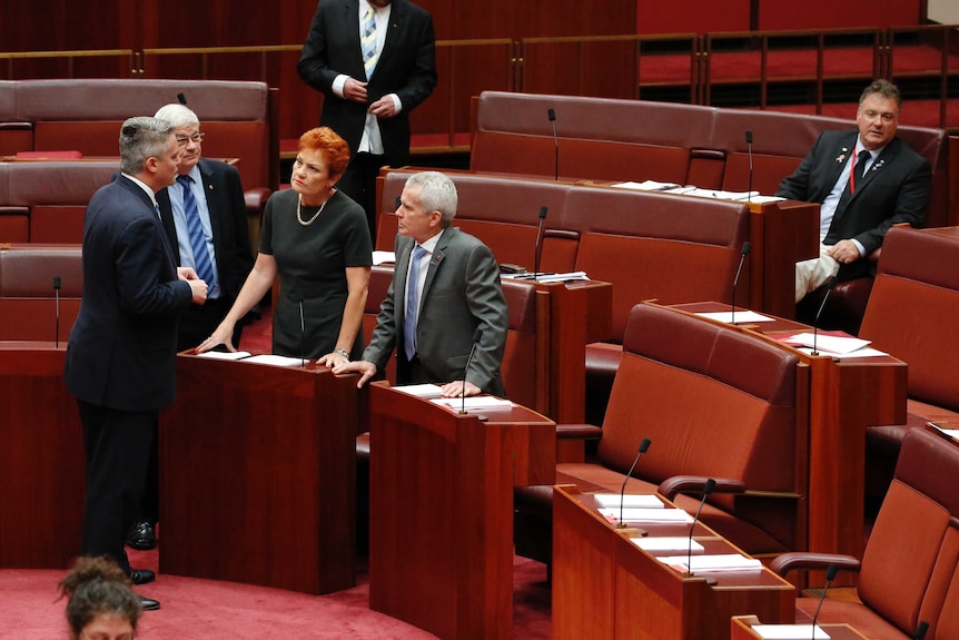 One Nation senators Pauline Hanson and Malcolm Roberts speak to Mathias Cormann, Rod Culleton sits alone.