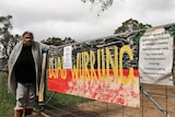 A woman standing next to a gate with signs emblazoned on it including 'Djab Wurrung'.