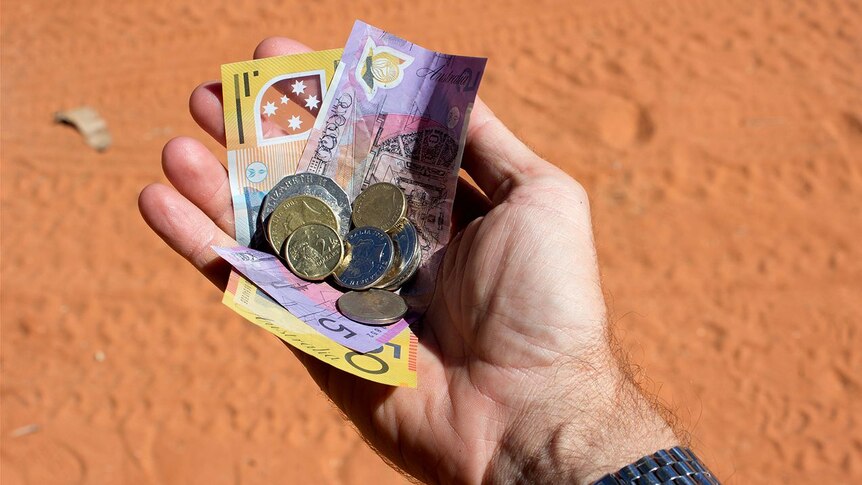 A hand holding a collection of Australian currency with dirt road in shot.