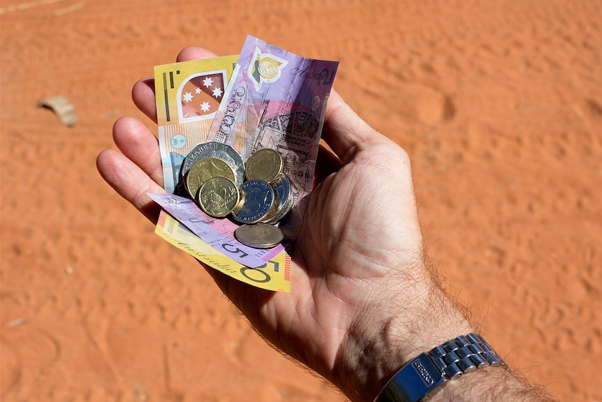 A hand holding a collection of Australian currency