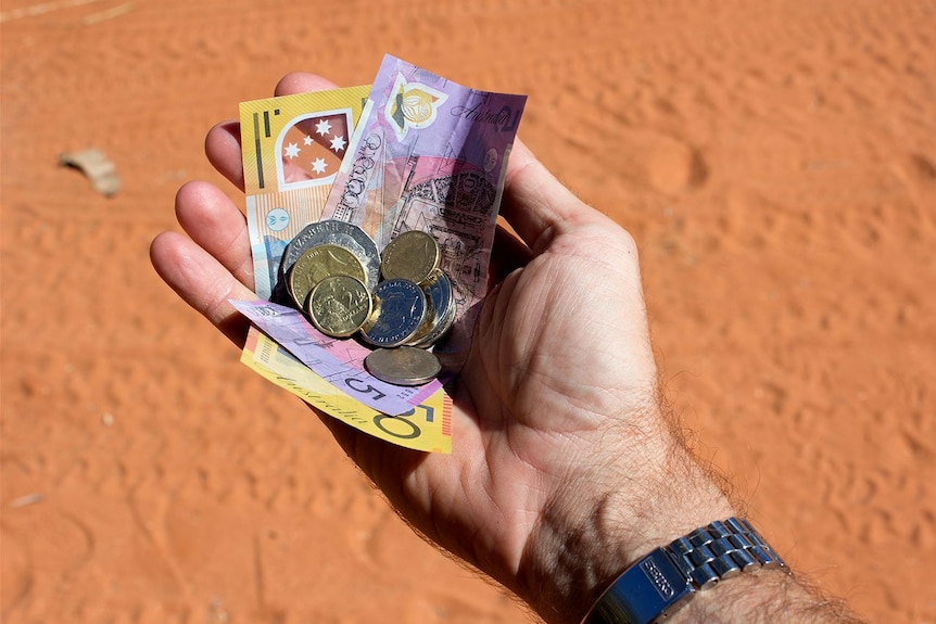 A hand holding a collection of Australian currency with dirt road in shot.