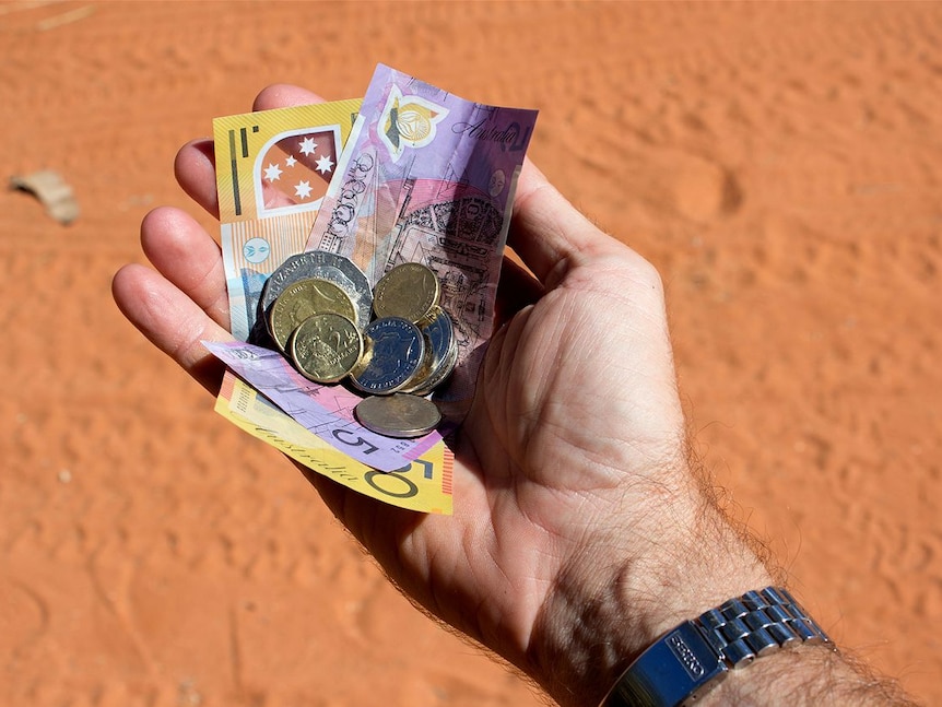 A hand holding a collection of Australian currency