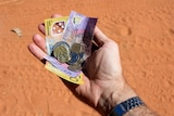 A hand holding a collection of Australian currency with dirt road in shot.