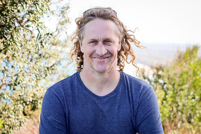 Man with long blond hair smiling from a lookout on the coast.