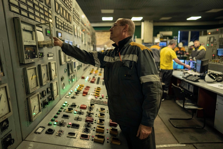 a power plant worker presses a button on a console inside a power plant